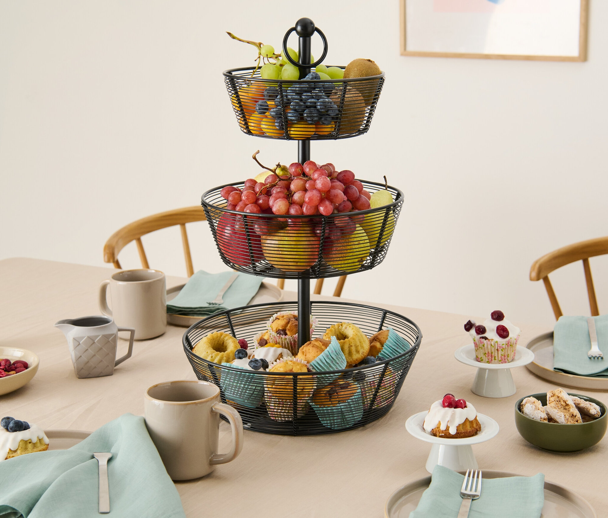 Na stole stojí trojposchodový etažér s ovocím a muffiny.