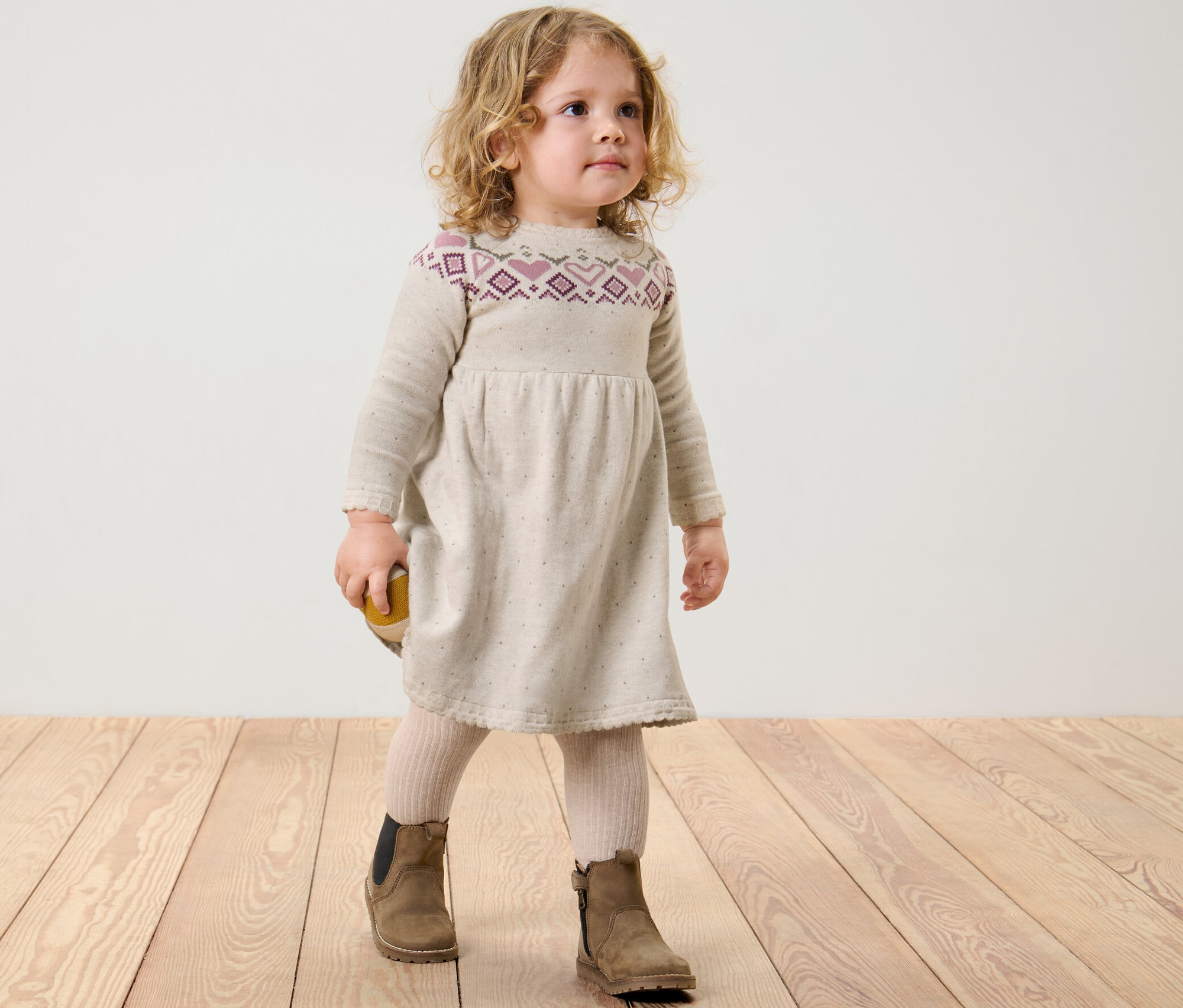 Dievča stojí na drevenej podlahe a má na sebe detské pletené šaty.