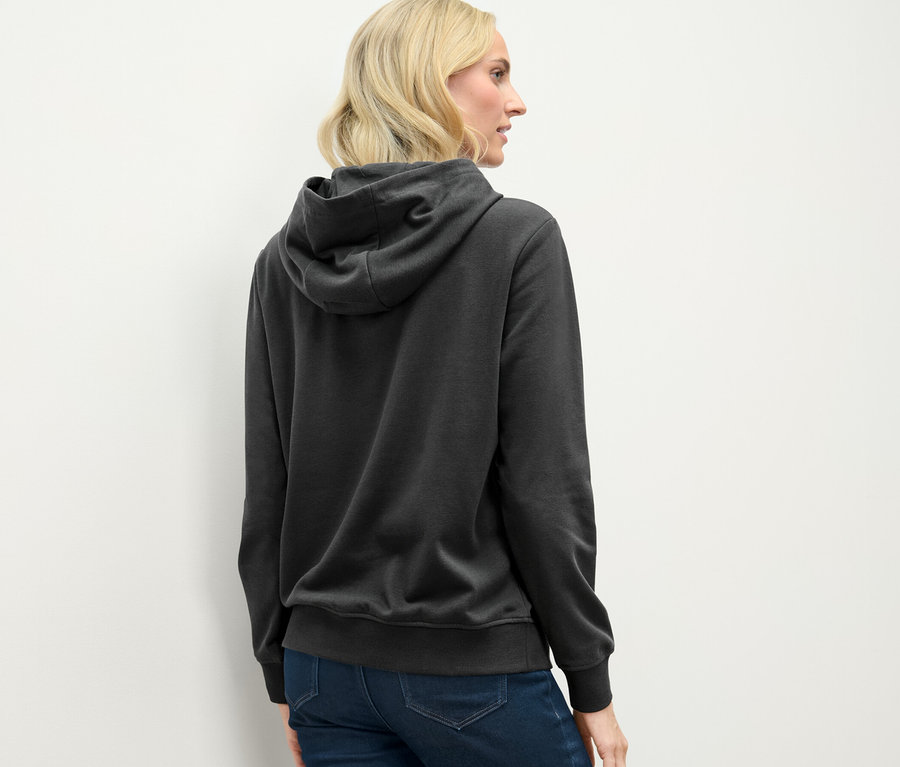 Zozadu je vidieť žena s blond vlasmi v antracitovej mikine s kapucňou.