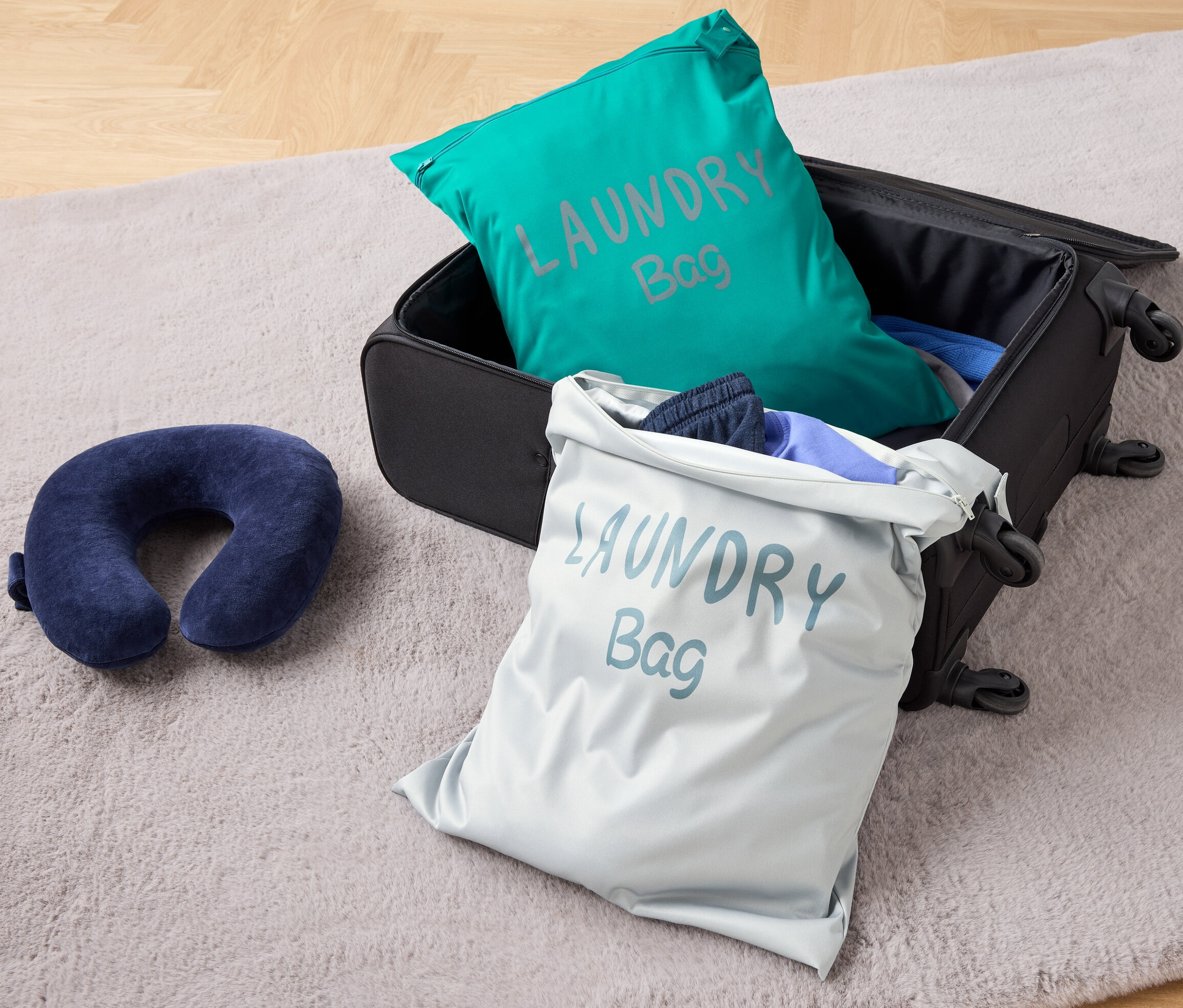 Na podlahe leží otvorený kufor s dvoma cestovnými ochrannými vreckami a cestovný vankúš.