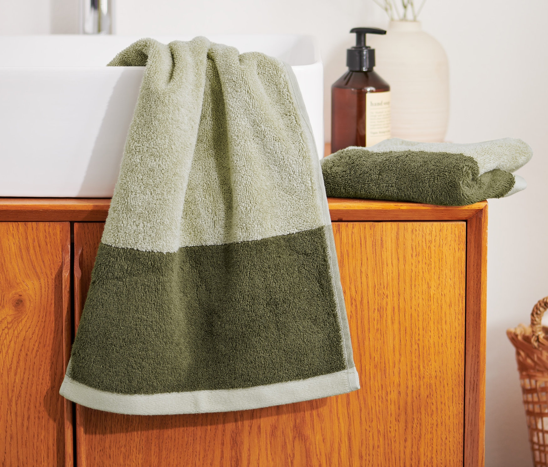 Na umývadle visí zelený uterák a vedľa neho ležia dva kvalitné žakárové uteráky pre hostí.