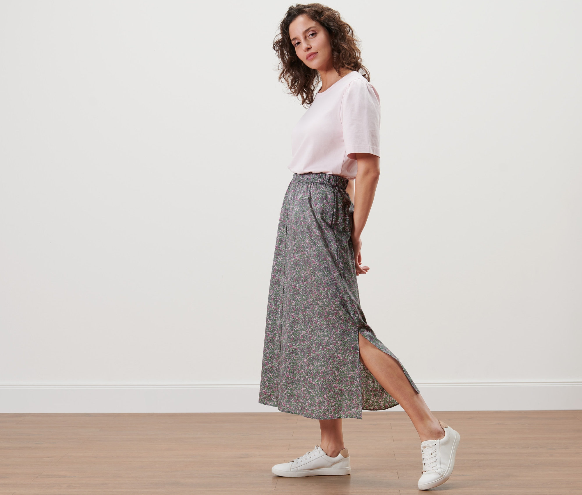 Žena pózuje v kvetinovej midi sukni a bielych teniskách.