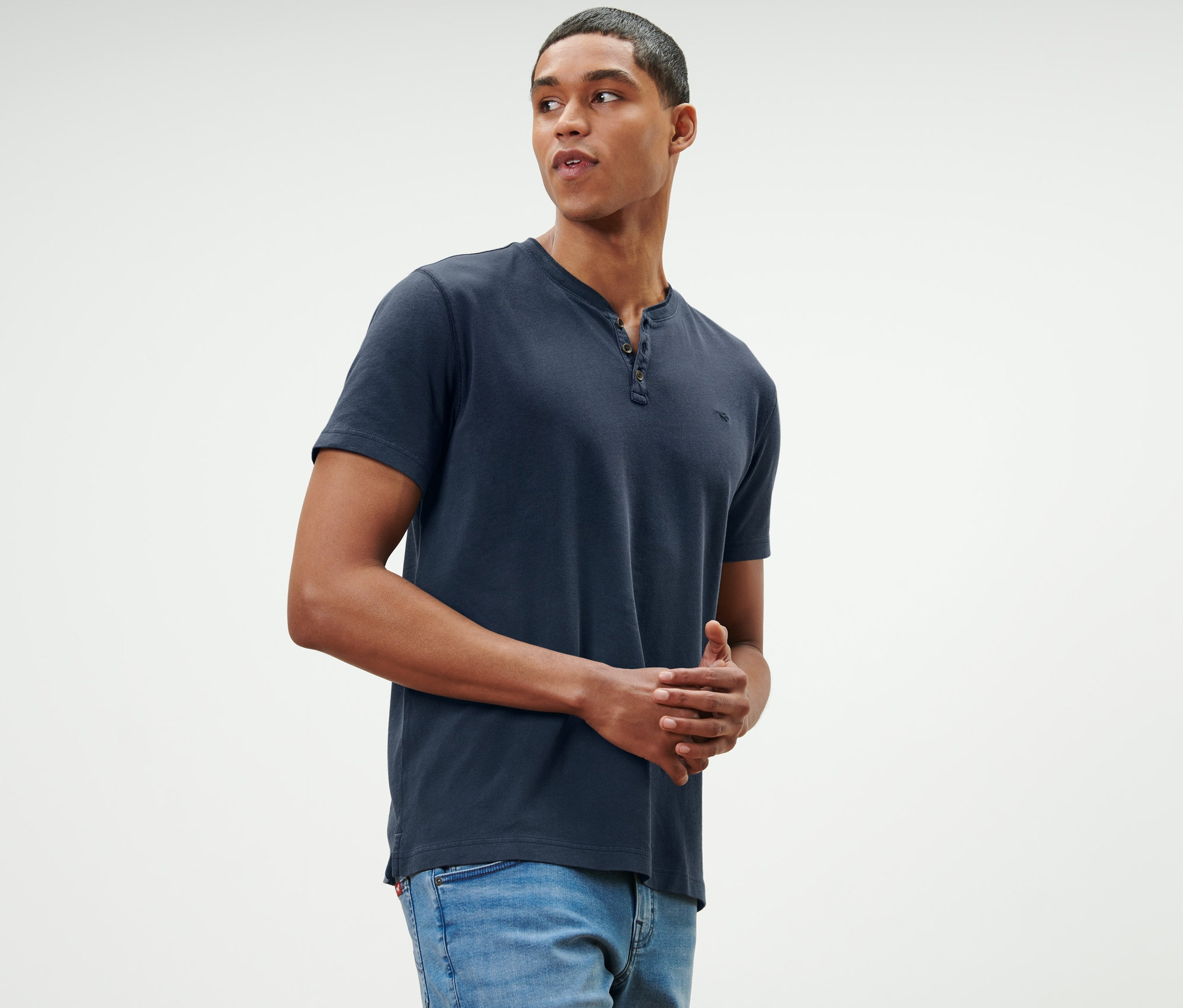 Muž pózuje v modrom tričku henley »Mustang« s krátkym rukávom a džínsoch.