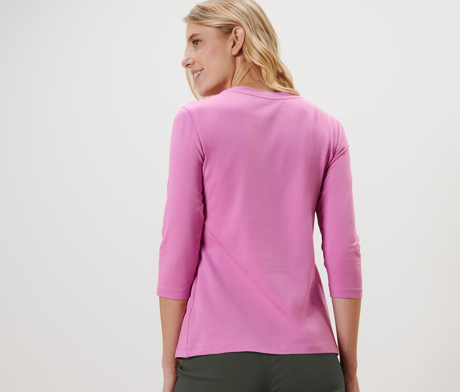 Žena sa pozerá cez rameno a má na sebe ružové tričko s trojštvrťovými rukávmi.