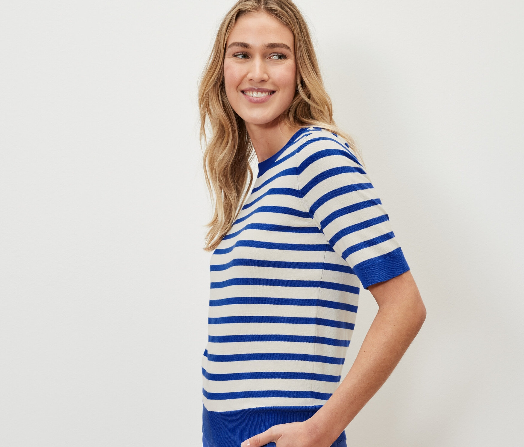 Žena má na sebe pruhovaný pulóver z jemného úpletu a modré nohavice.