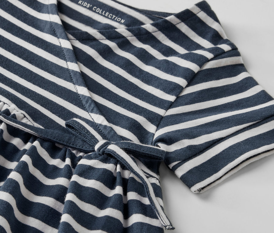 Detail detských džersejových šiat s modrými a bielymi pruhmi a viazaním v páse.