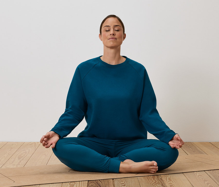 Žena sedí v tureckom sede na podložke na jogu a medituje.