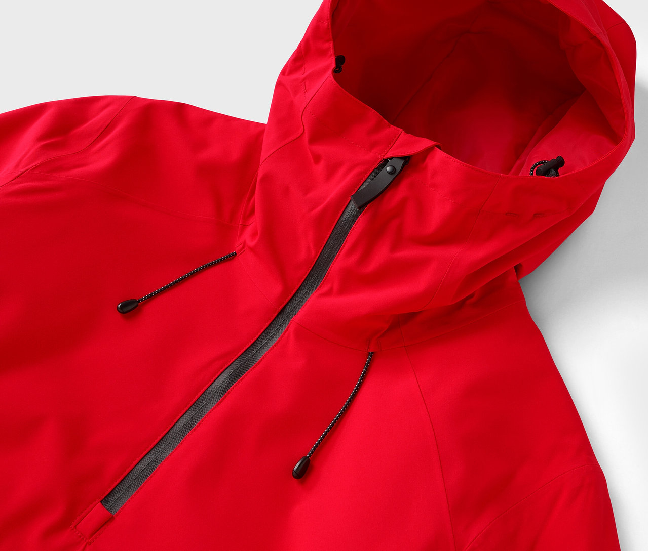 Detail červenej bundy s kapucňou a čiernym zipsom.