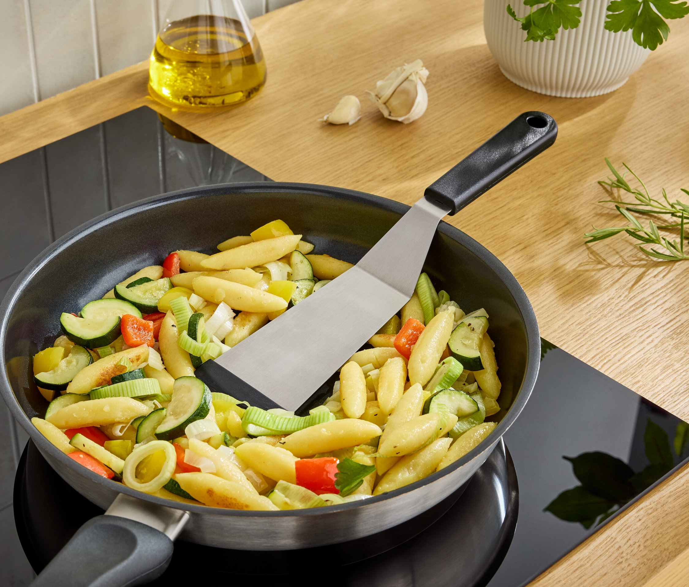 Špachtľa obracia halušky so zeleninou na panvici na sporáku.