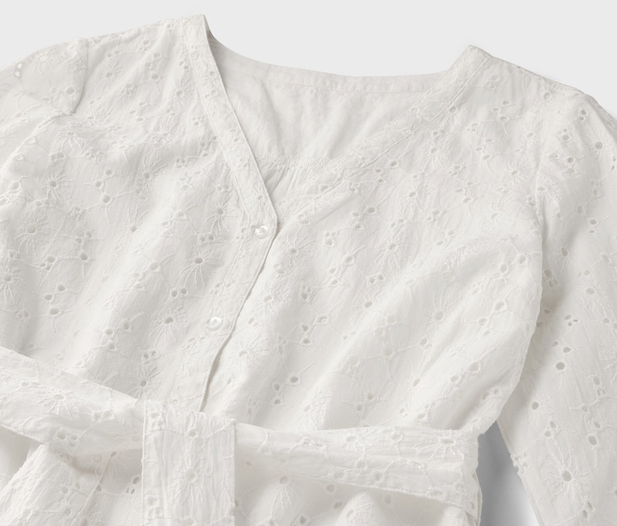 Detail bielych blúzkových šiat s dierkovanou výšivkou.