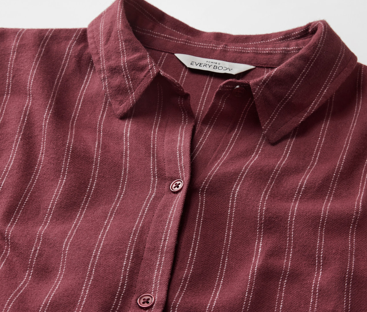 Detail bordovej košele s prúžkami, golierom a gombíkmi.