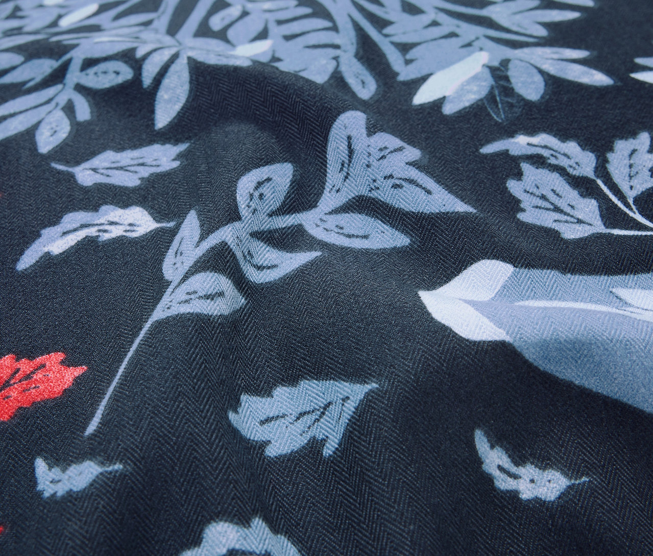 Detailný záber na tmavomodrú látku s potlačou listov a kvetov v odtieňoch modrej a červenej.