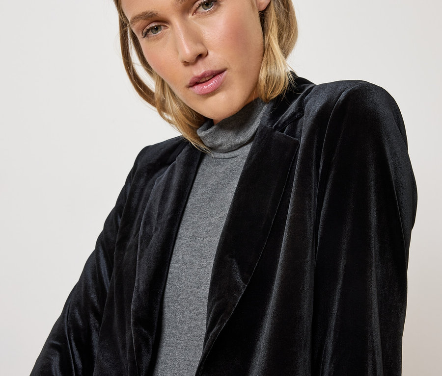 Žena má na sebe čierny zamatový blejzer a sivý rolák.