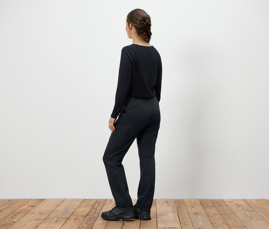 Žena v čiernom svetri a nohaviciach stojí chrbtom ku kamere.