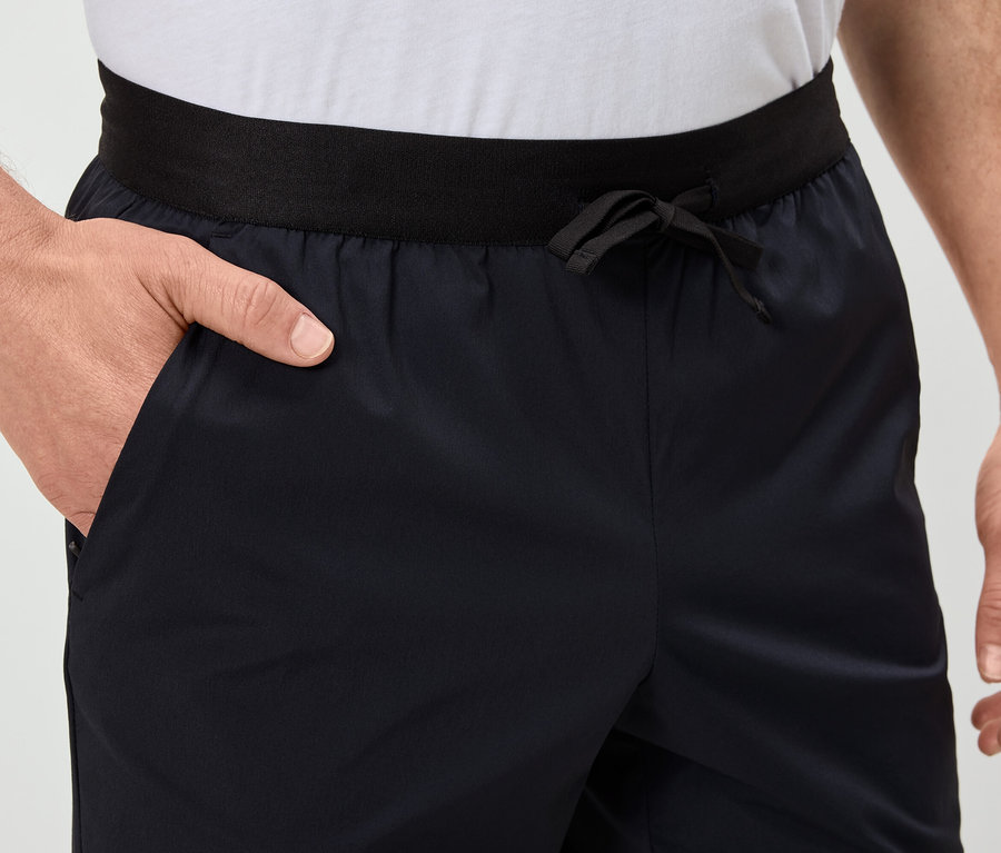 Muž má ruku vo vrecku tmavomodrých šortiek s čiernym pásom.