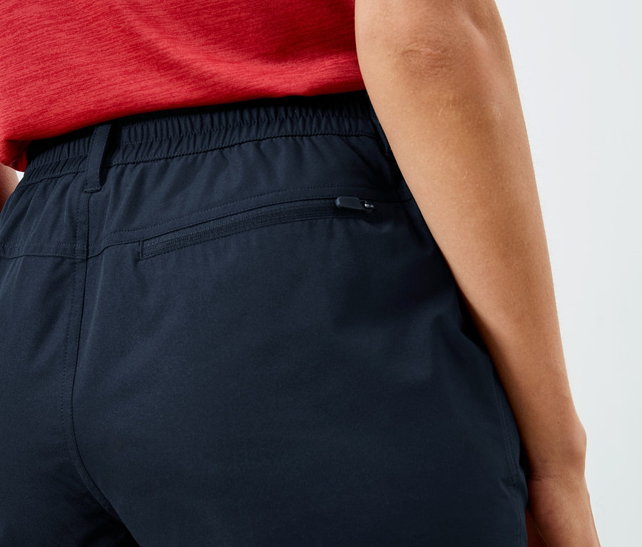 Detailný záber na zadnú časť osoby v tmavomodrých nohaviciach s elastickým pásom a vreckom na zips.