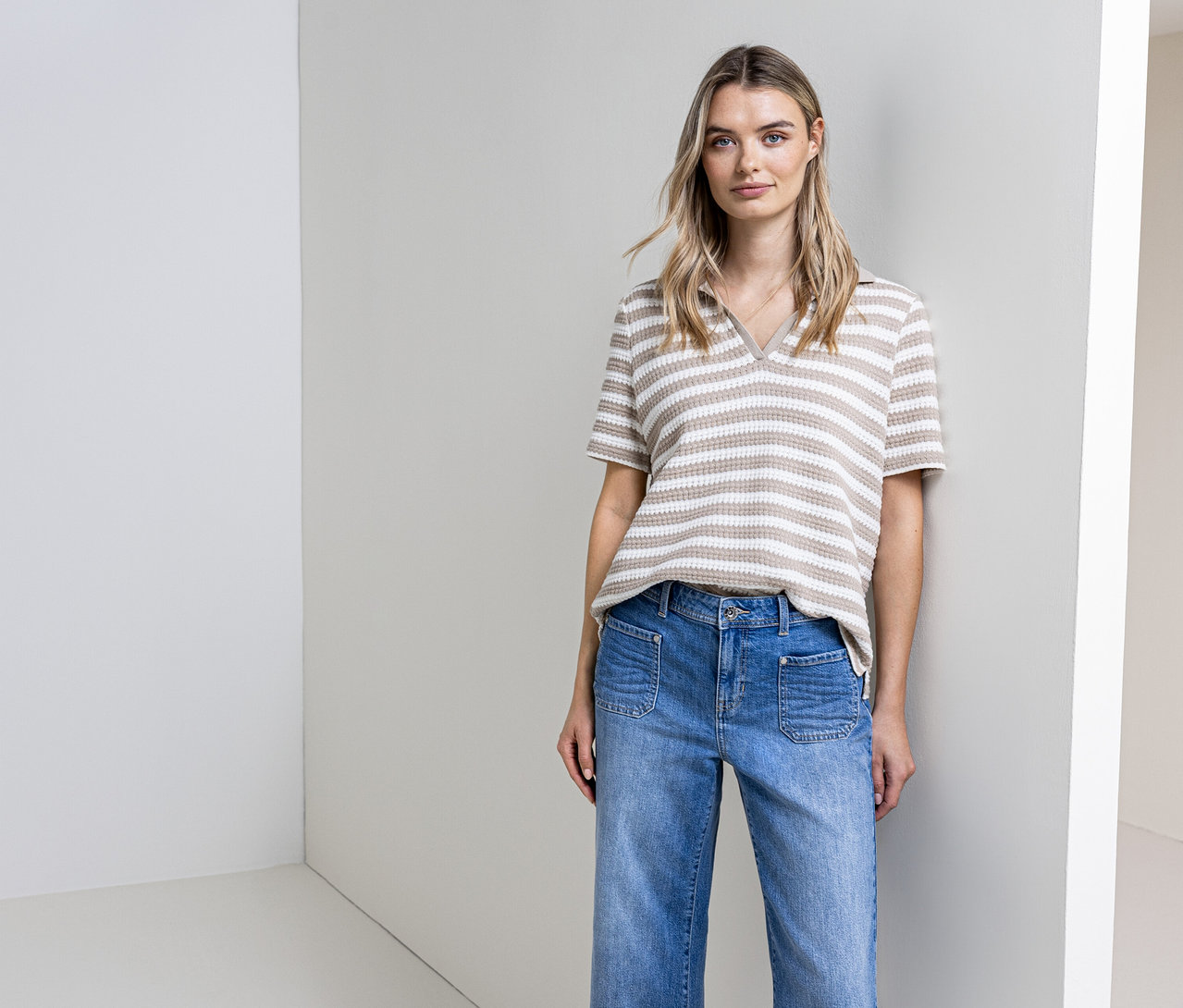 Žena pózuje v džínsoch a pruhovanom tričku z úpletu Street One pred stenou.