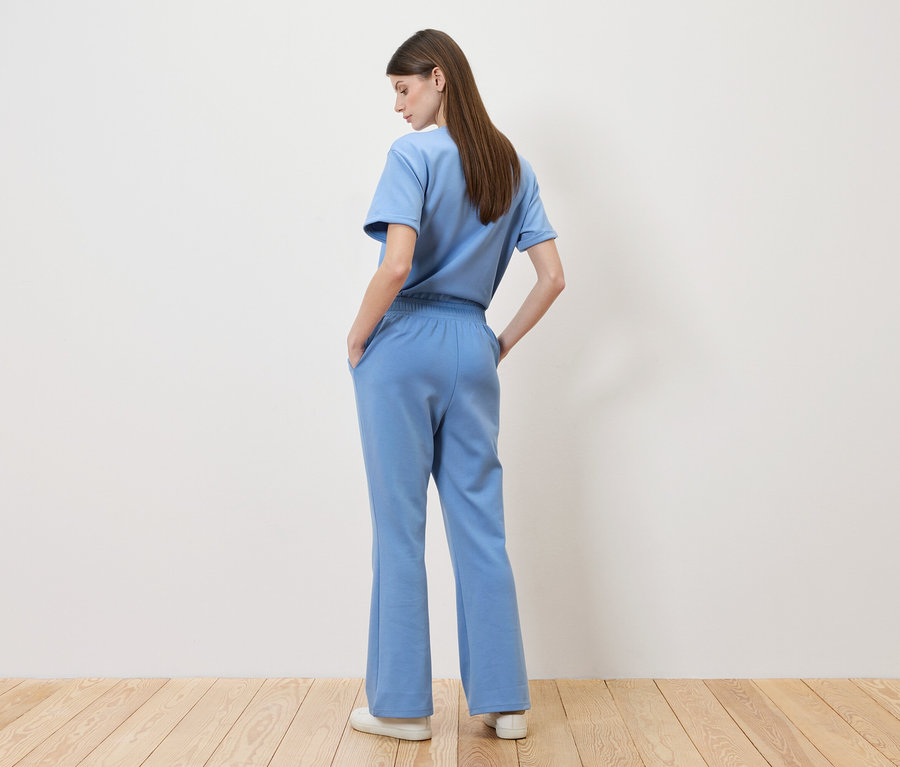 Žena stojí chrbtom k fotoaparátu, má na sebe svetlomodré tričko a zodpovedajúce nohavice