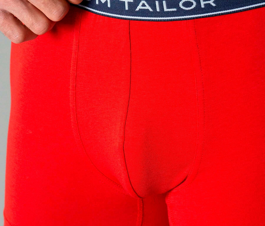 Muž má na sebe červené boxerky s tmavomodrým pásom s nápisom „TOM TAILOR“.