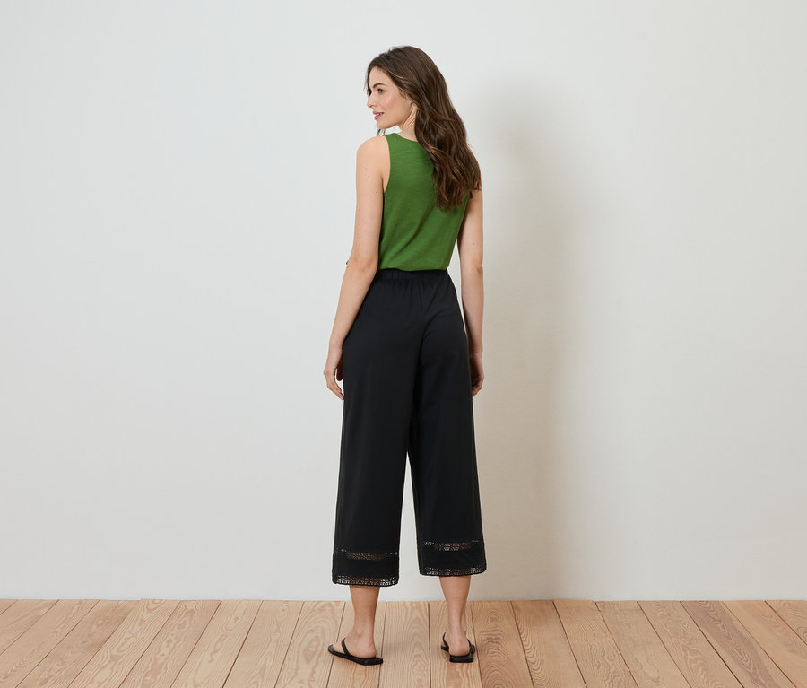 Žena stojí chrbtom k fotoaparátu, má na sebe zelený top a čierne culottes s čipkou na spodnej časti.