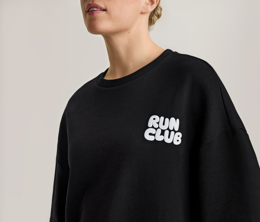 Žena má na sebe čiernu mikinu s bielym nápisom "RUN CLUB".