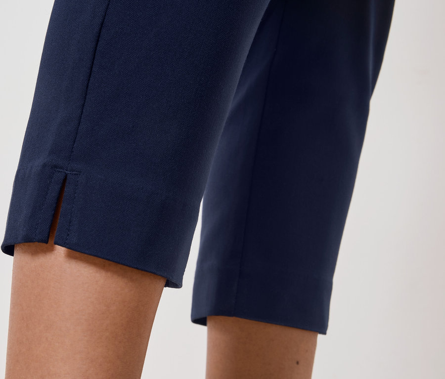 Detailný záber na nohy osoby, ktorá má na sebe tmavomodré nohavice s rozparkom na leme.