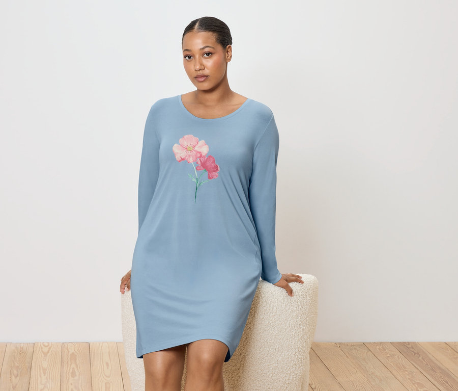 Žena sedí na stoličke a má na sebe modrú nočnú košeľu s kvetinovým vzorom.