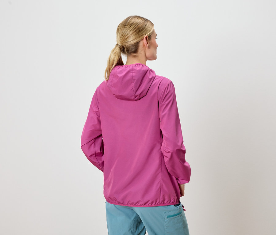 Pohľad zozadu na ženu s blond vlasmi, ktorá má na sebe ružovú bundu s kapucňou a modré nohavice.