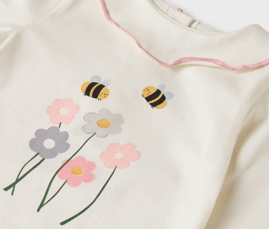 Detailný pohľad na krémový top s ružovým volánikovým golierom, zdobený kvetinovými a včelími motívmi.