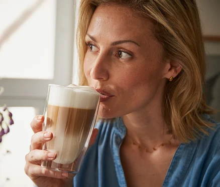 Žena pije latte macchiato z dvojstenného pohára.