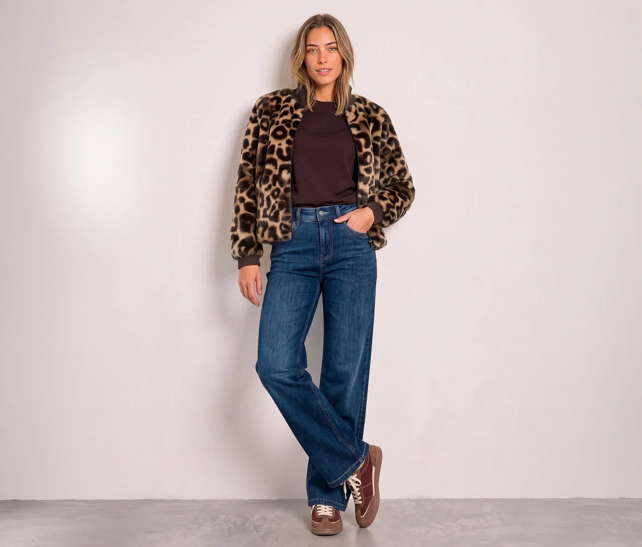 Žena má na sebe Street One Blouson s leopardím vzorom, hnedý top, široké džínsy a hnedé šnurovacie topánky.