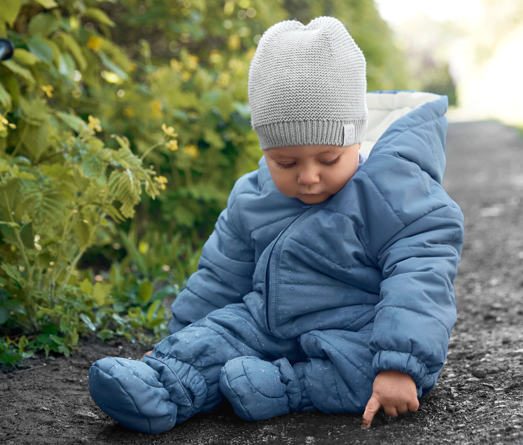 Dieťa sedí na zemi v modrom zimnom overale a pletenej čiapke.