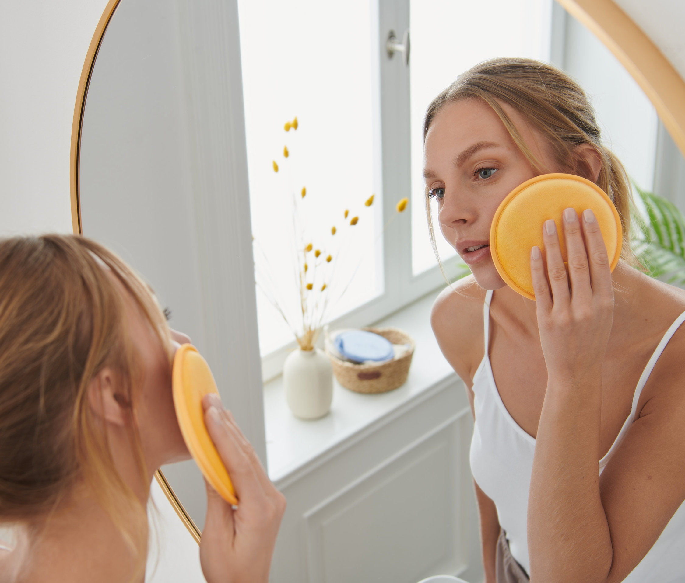 Žena si čistí tvár XL odličovacím tampónom na opakované použitie, modrý, žltý a hnedý.