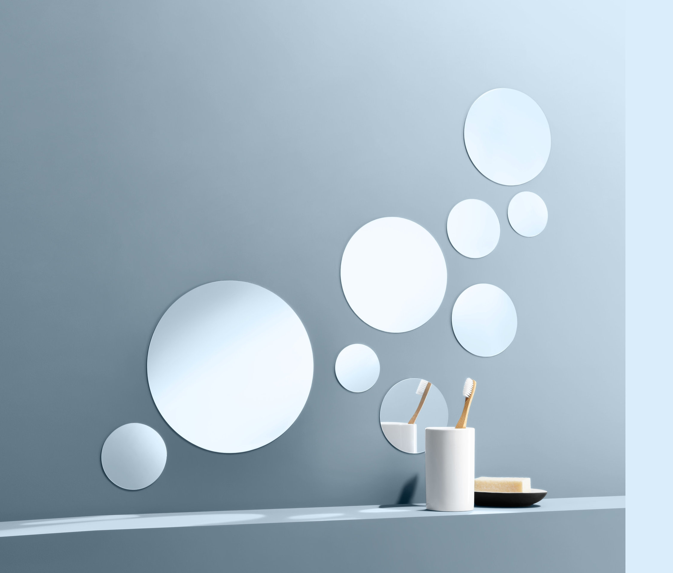 Na modrej stene je umiestnených deväť samolepiacich zrkadlových nálepiek. Na poličke stojí pohár s dvoma zubnými kefkami a mydlo na tanieriku.