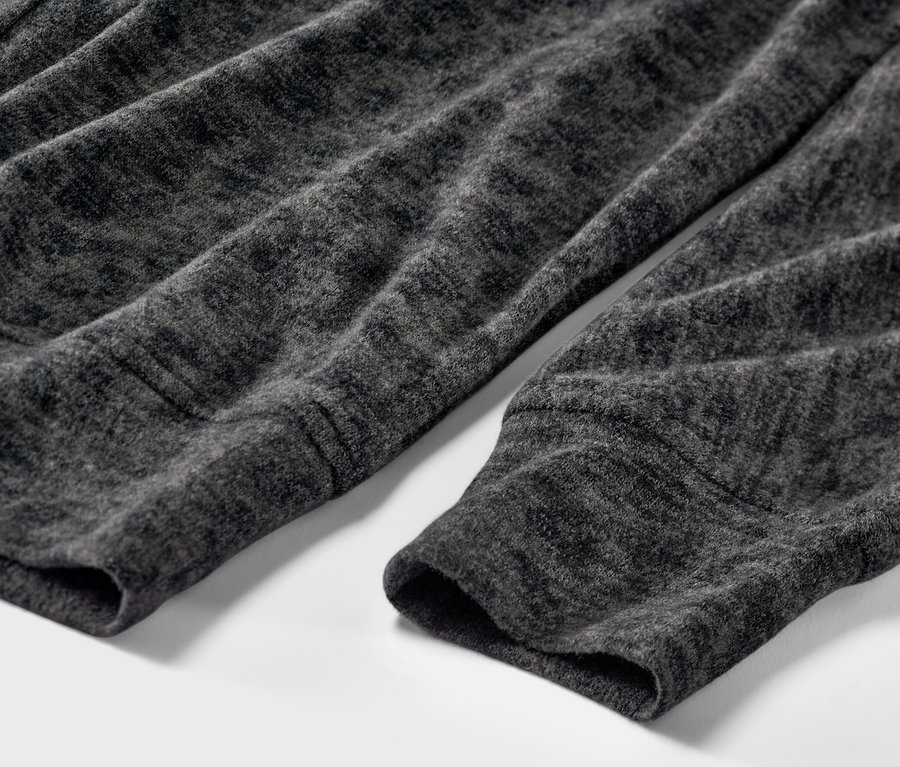 Detail šedého trička s netopierími rukávmi s potlačou.