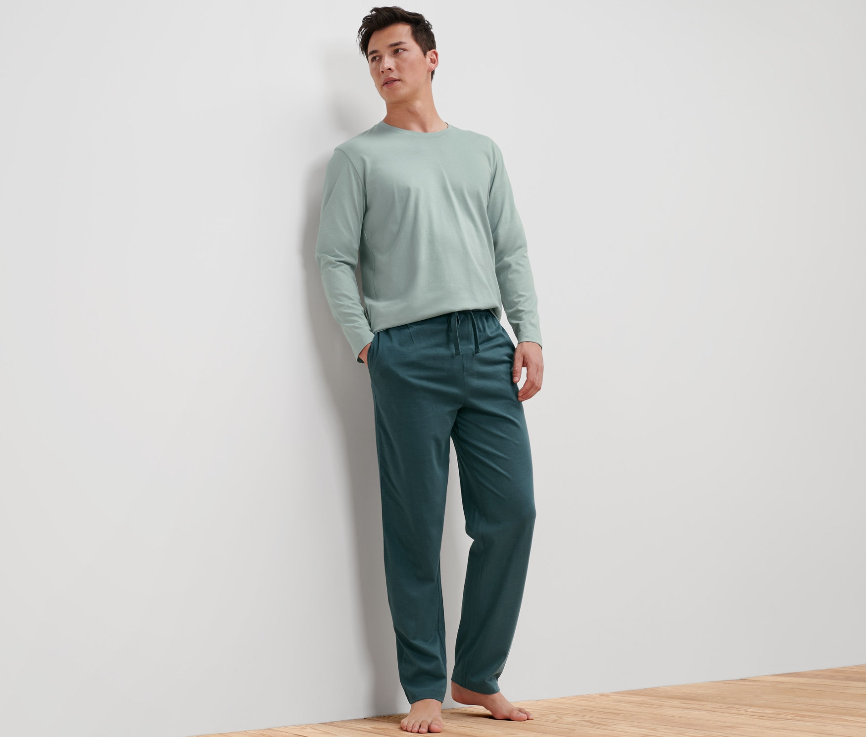 Muž opretý o stenu má na sebe pánske pyžamo.