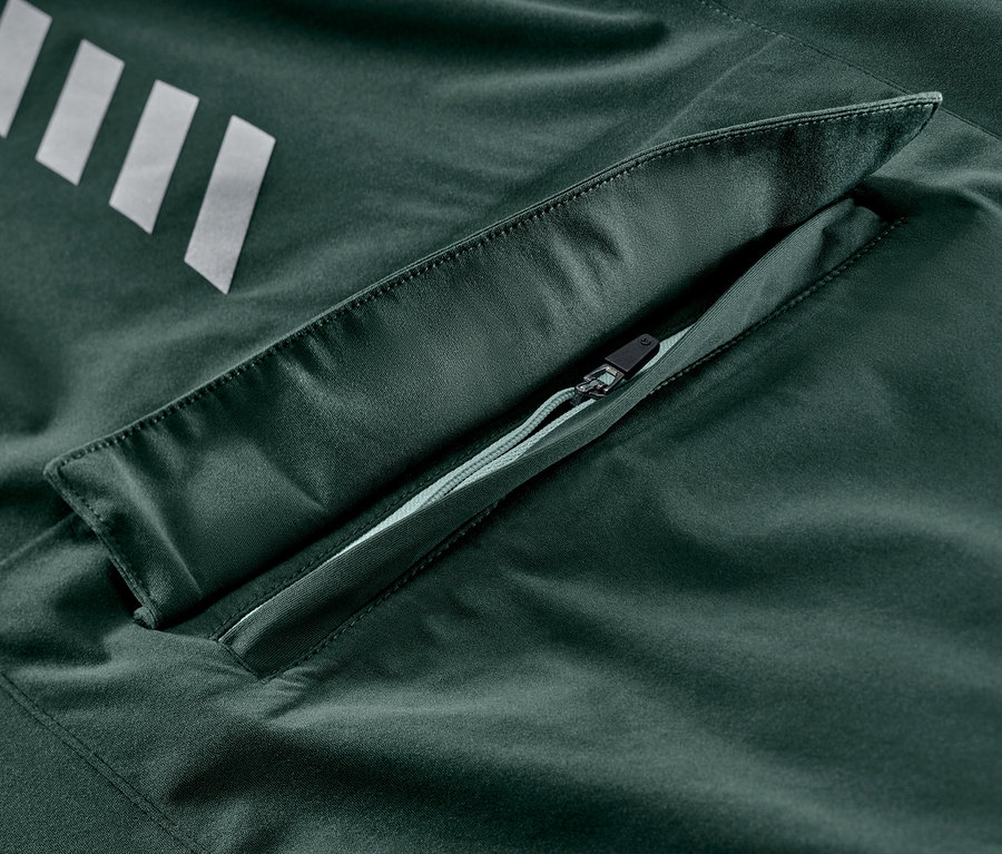 Detail cyklistickej bundy do dažďa so striebornými pruhmi a vreckom na zips.