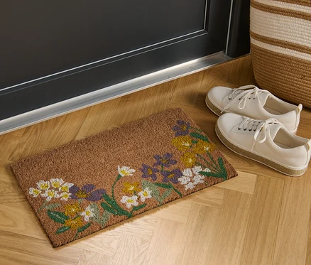 Kokosová rohožka s kvetinovým motívom leží pred dverami.