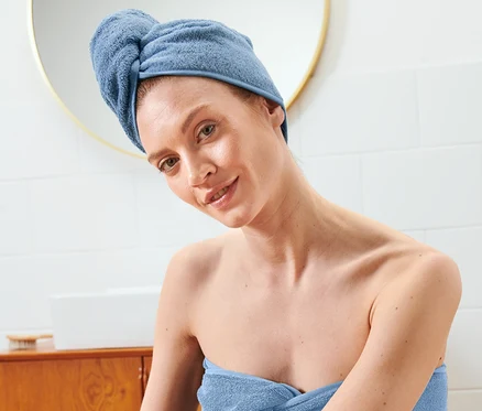 Žena sedí zabalená v uteráku s uterákovým turbanom na hlave.