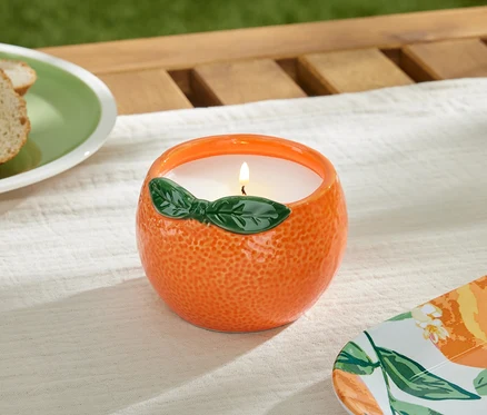 Horiaca sviečka citronela v oranžovej nádobe na stole.