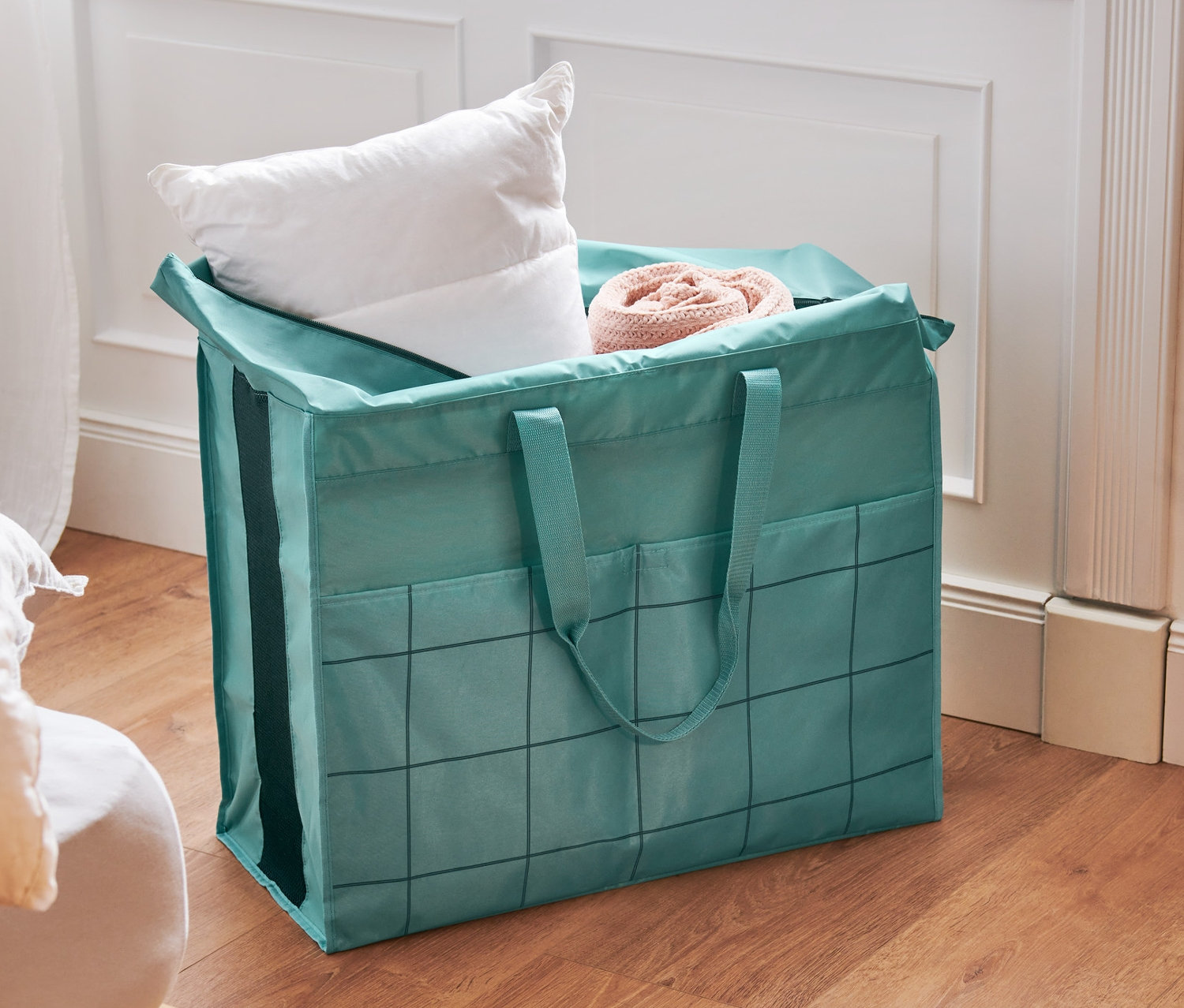 Zelená taška na lôžkoviny Veľká taška na lôžkoviny stojí na podlahe vedľa postele.