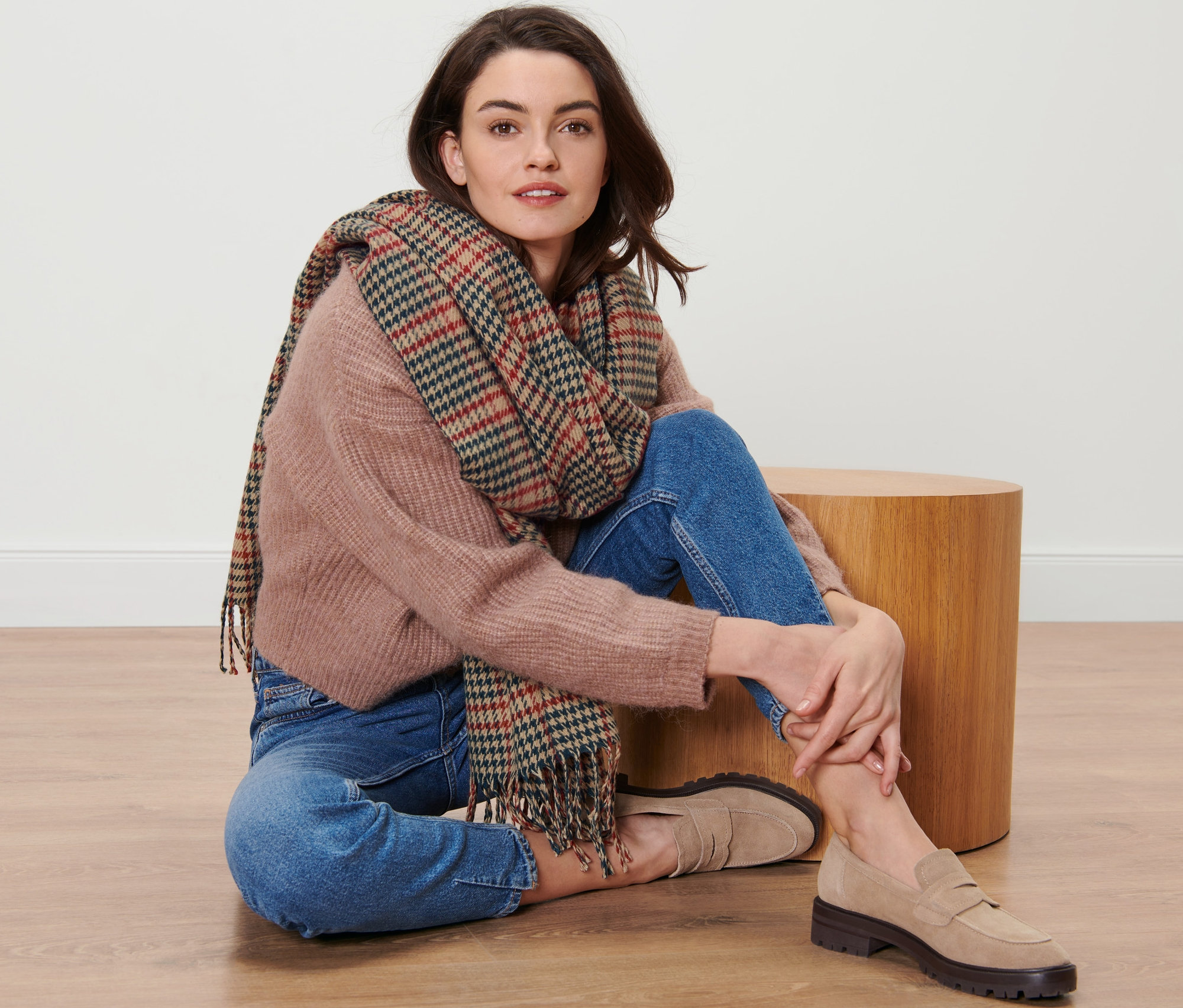 Žena sedí na podlahe a má na sebe kockovaný tkaný šál.