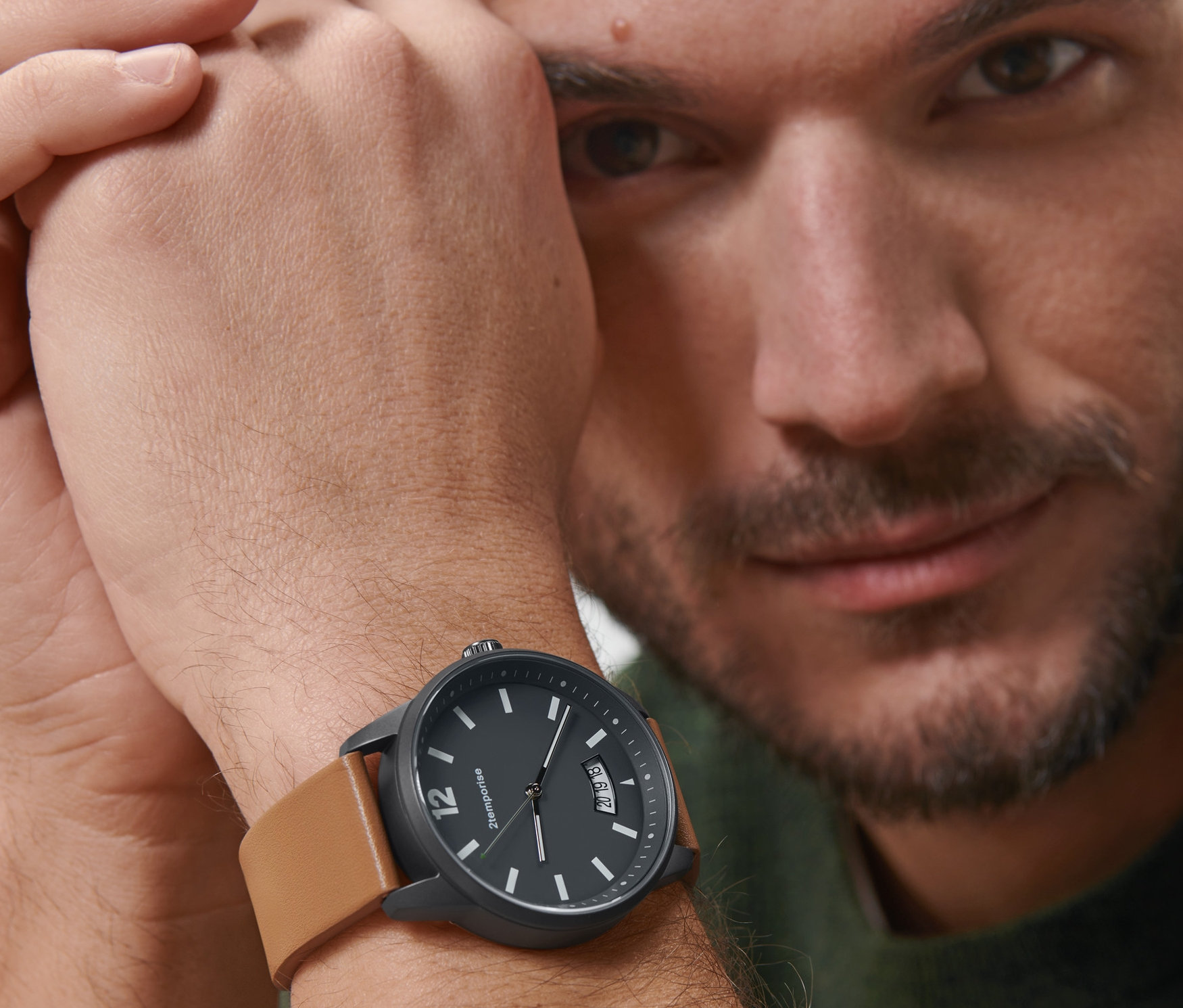 Muž sa pozerá do kamery a na zápästí má čierne náramkové hodinky v pilotskom štýle s hnedým koženým remienkom.