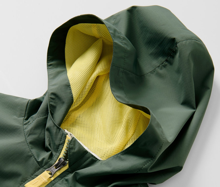 Detail zelenej detskej športovej funkčnej bundy s kapucňou a žltým zipsom.