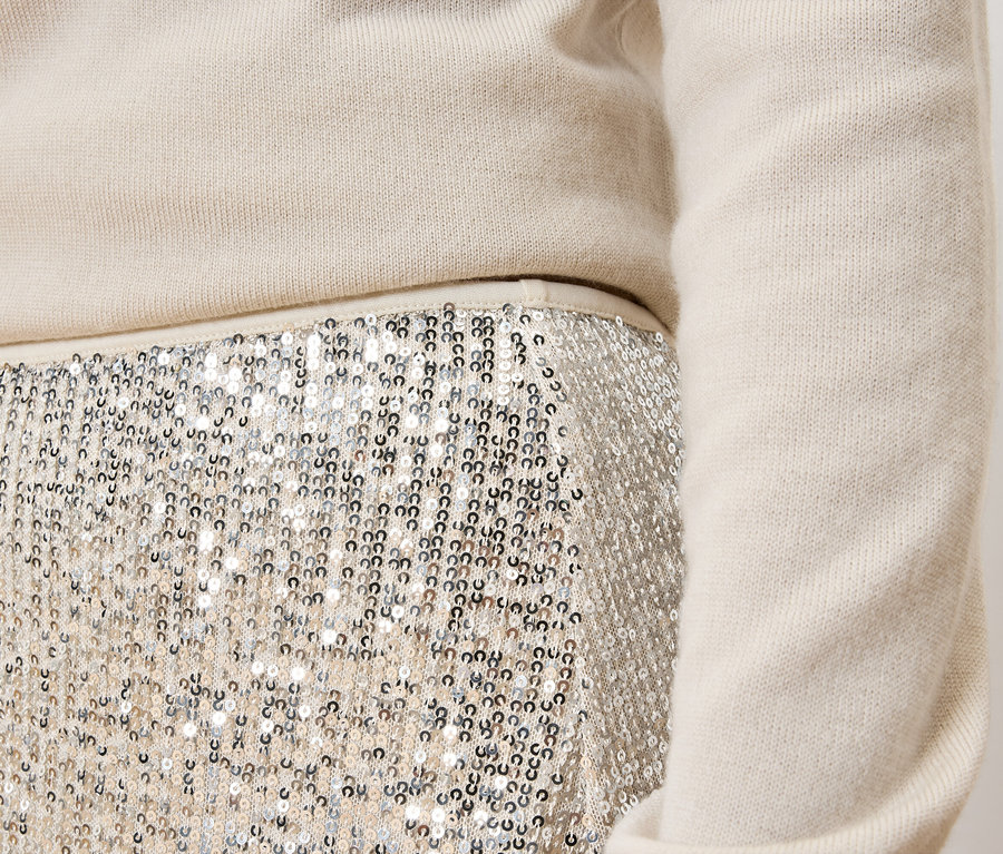 Detail dámskeho outfitu: krémový sveter a strieborná flitrová sukňa.