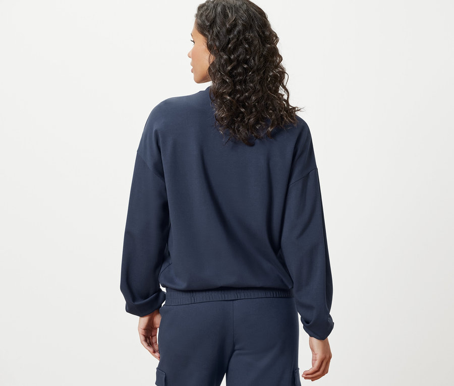 Zozadu je vidieť žena s tmavými vlnitými vlasmi v tmavomodrej mikine.