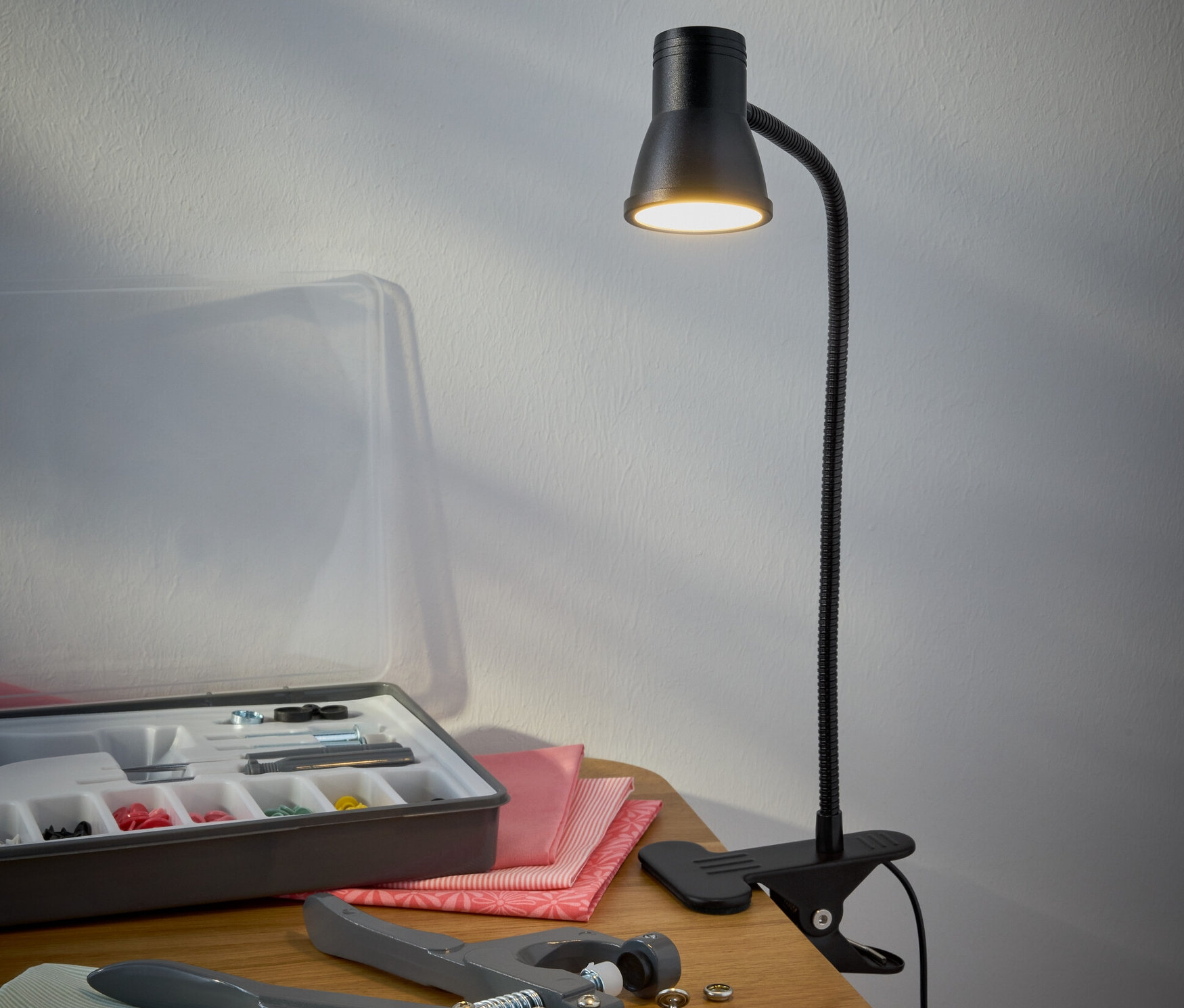 Čierna LED lampa s klipom stojí na stole vedľa súpravy na šitie.