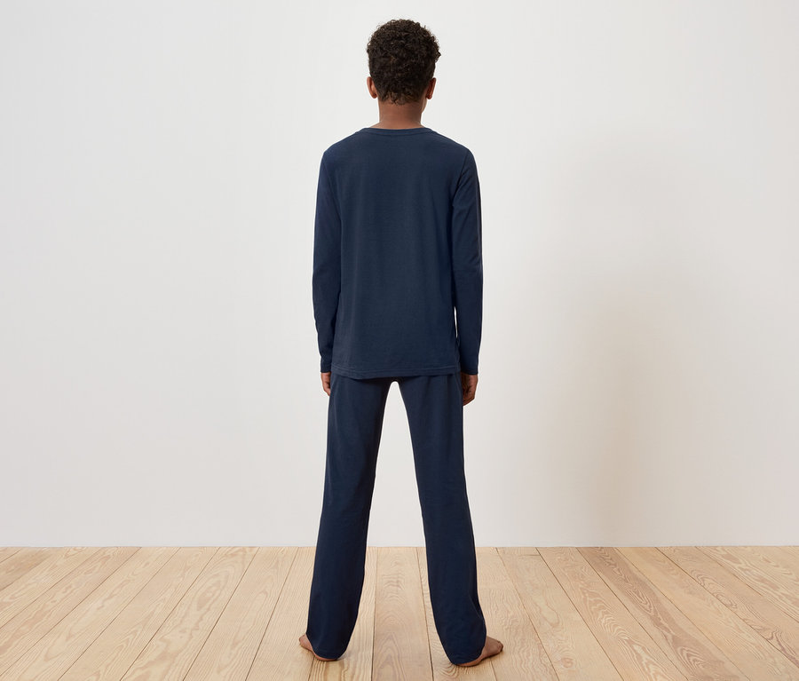 Osoba stojí chrbtom k fotoaparátu a má na sebe tmavomodré pyžamo.