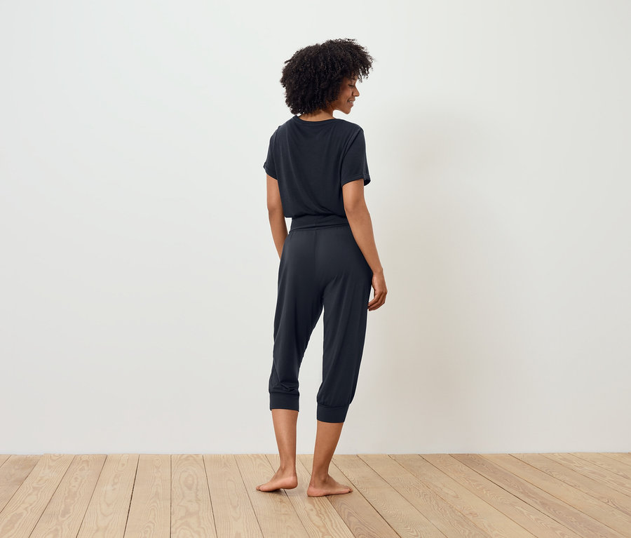 Žena v tmavom tričku a trojštvrťových nohaviciach stojí chrbtom ku kamere.