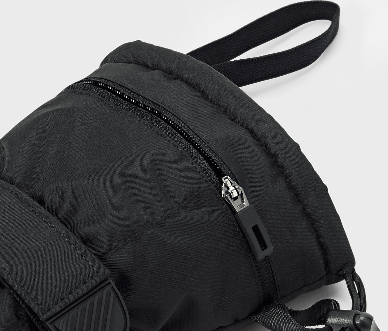 Detail čierneho batohu so zipsom a popruhom.